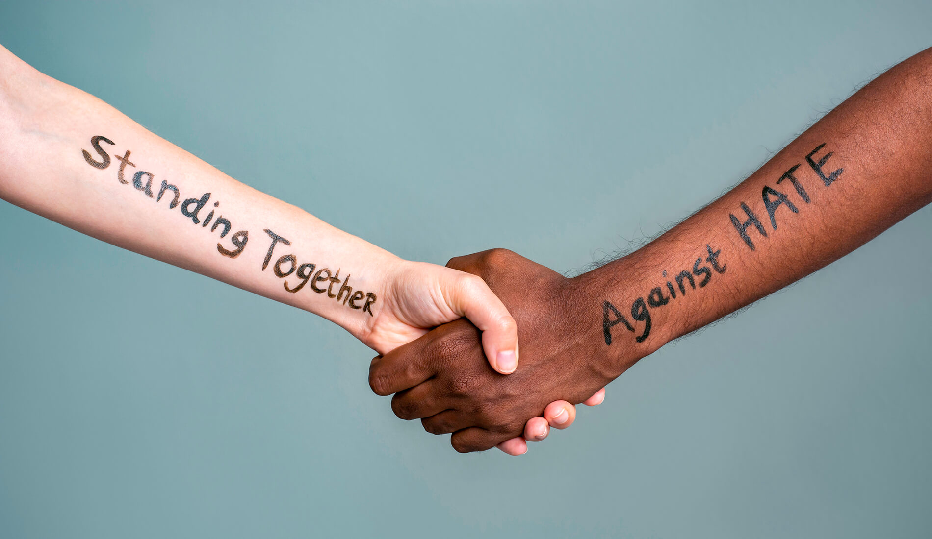hands clasping, one reads "standing together" and the other reads "against racism"